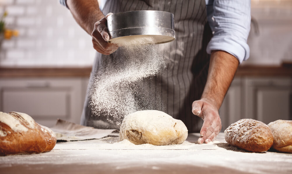 baker sieving flour over dough