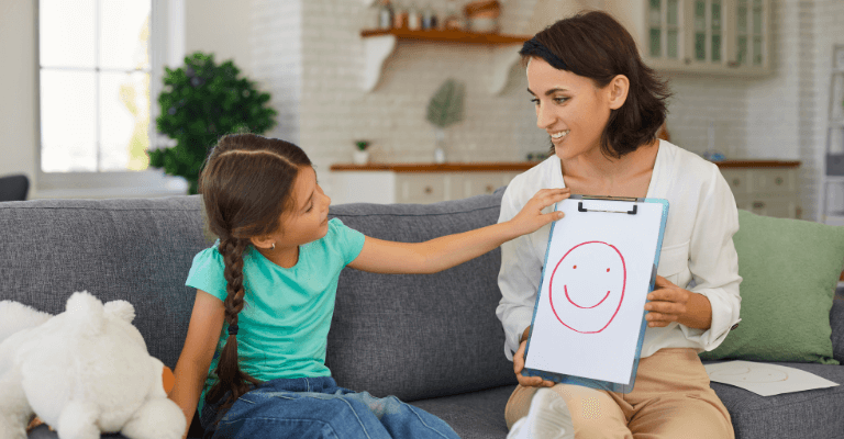 Child counseling session with a therapist showing a smiley face drawing to a young girl, highlighting child counseling and emotional support.