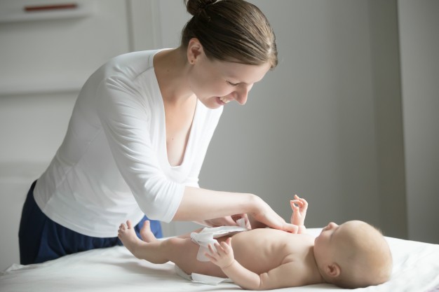 Young smiling beautiful woman fixing diaper of a newborn