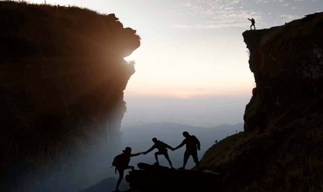 2 people helping another 1 climb a mountain peak