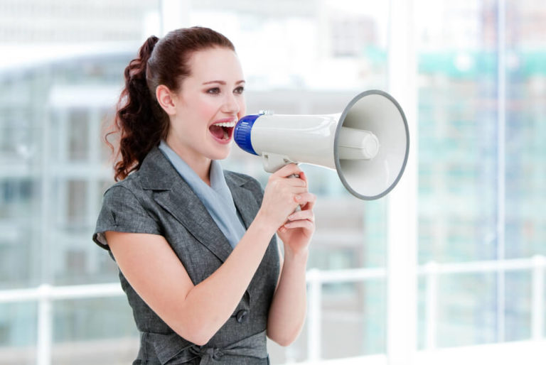 Self-assured businesswoman making herself heard through a megaphone standing in the office, assertive communication skills activities