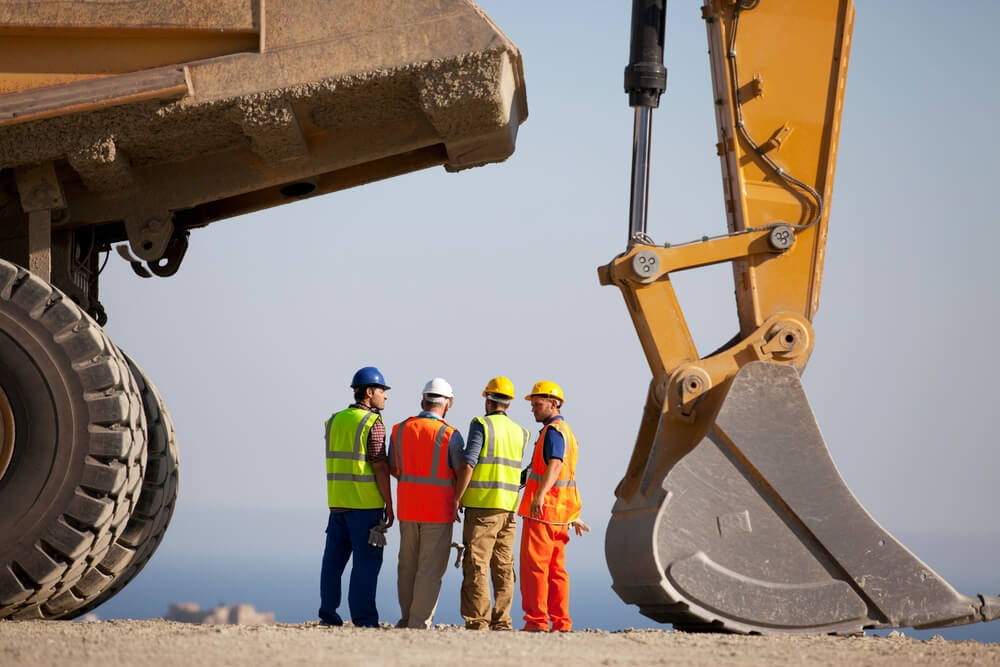 Project builders discussing a digging project with an excavator machine in front of them