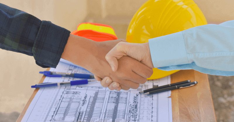 "Construction workers shaking hands on a project site"