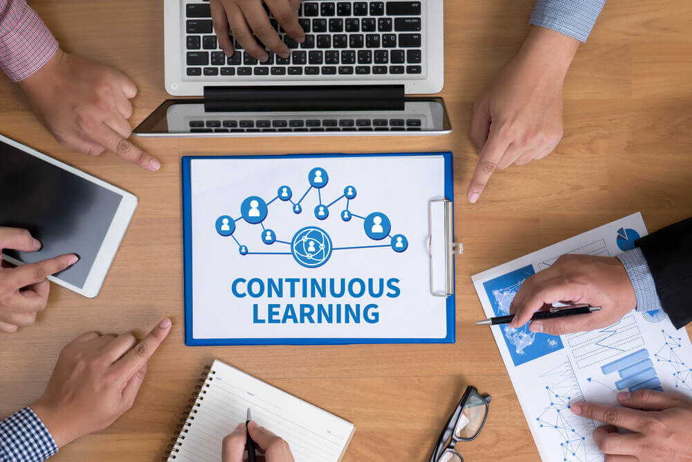 Image showing examples of continuous and lifelong learning, including books, a laptop, and a person taking notes.