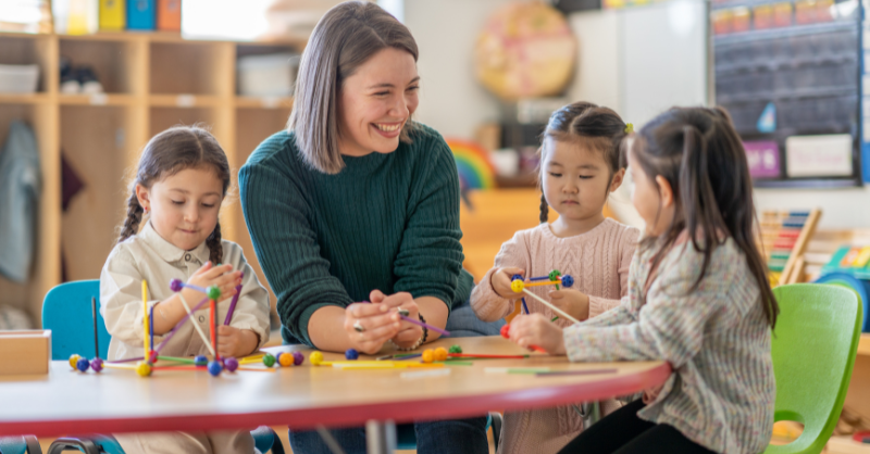 Teacher development in a classroom setting with a teacher engaging with young students in hands-on learning activities using colorful educational toys