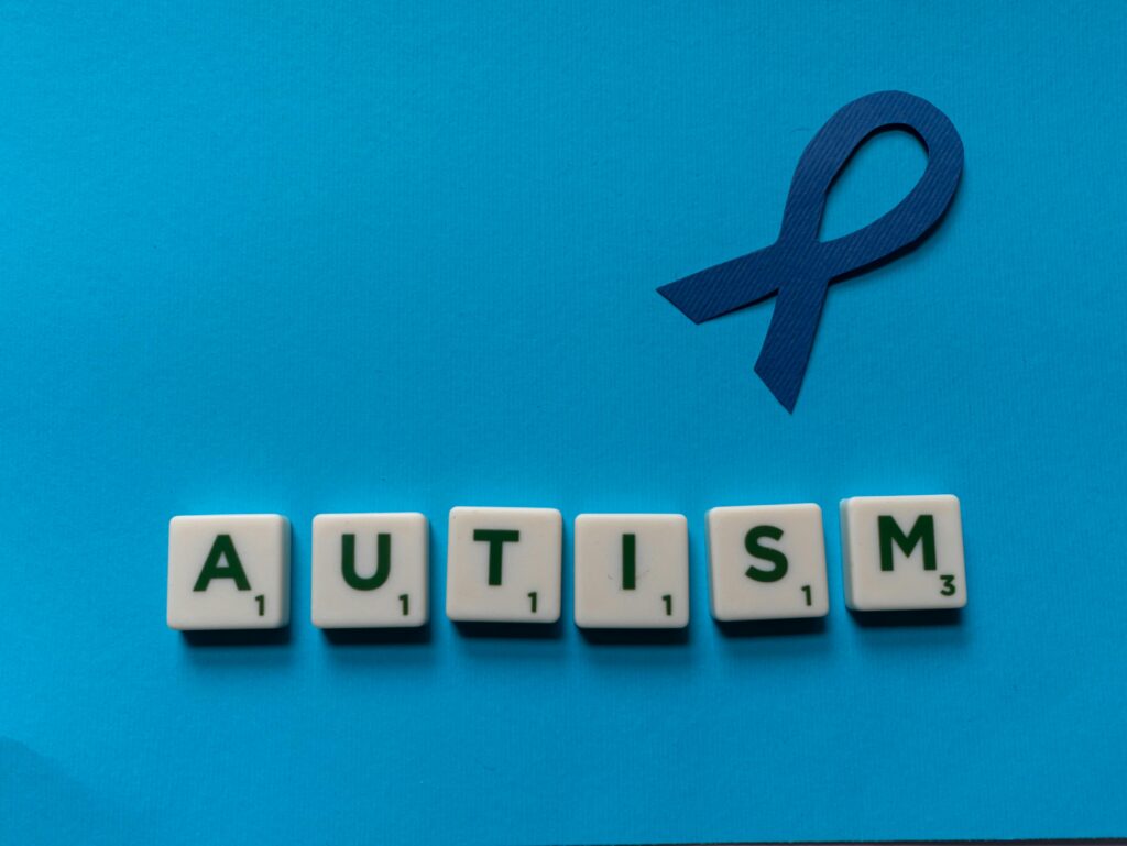 Flat lay of scrabble tiles spelling autism with a blue ribbon on a blue background.