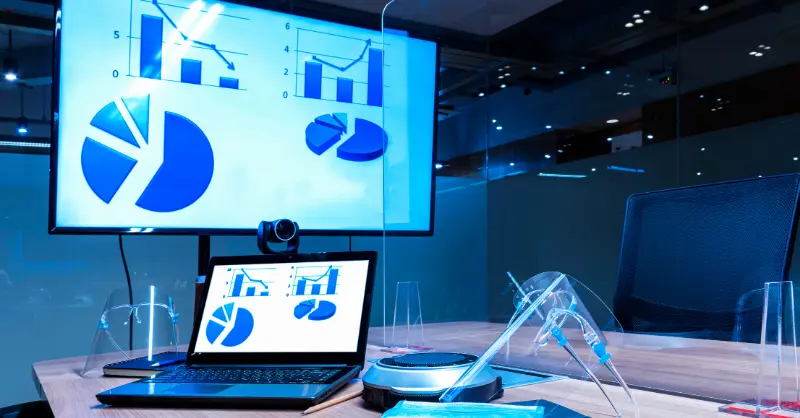 Basic Microsoft PowerPoint presentation showing pie charts and analytics on a large screen during a team meeting