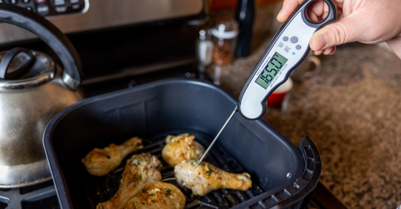 Checking cooked chicken's temperature with a digital thermometer to ensure it reaches 165°F (75°C) for food safety.
