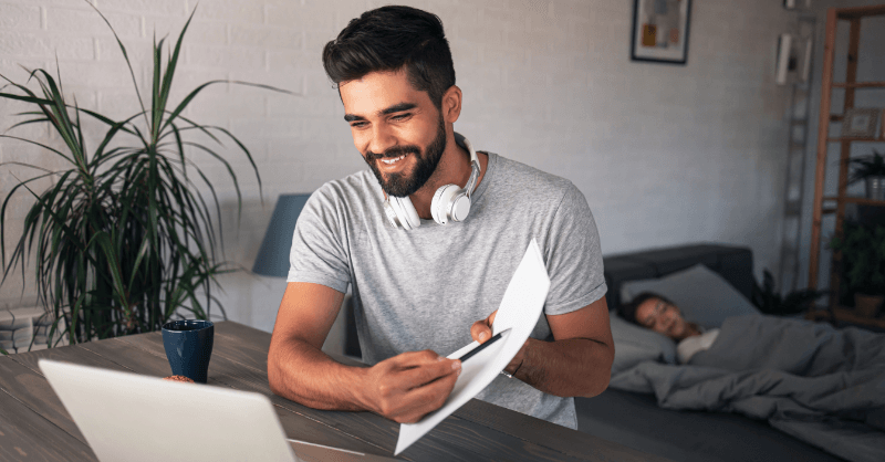 Teacher exploring freelance opportunities from home, working on a laptop with headphones in a cozy living space.